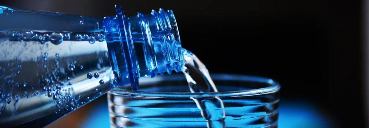 Water being poured from a bottle into a glass against a blue background