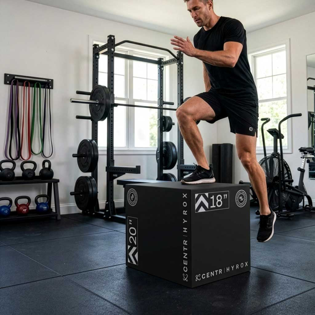 Man in black sportswear jumps onto a black foam plyometric box in a gym.
