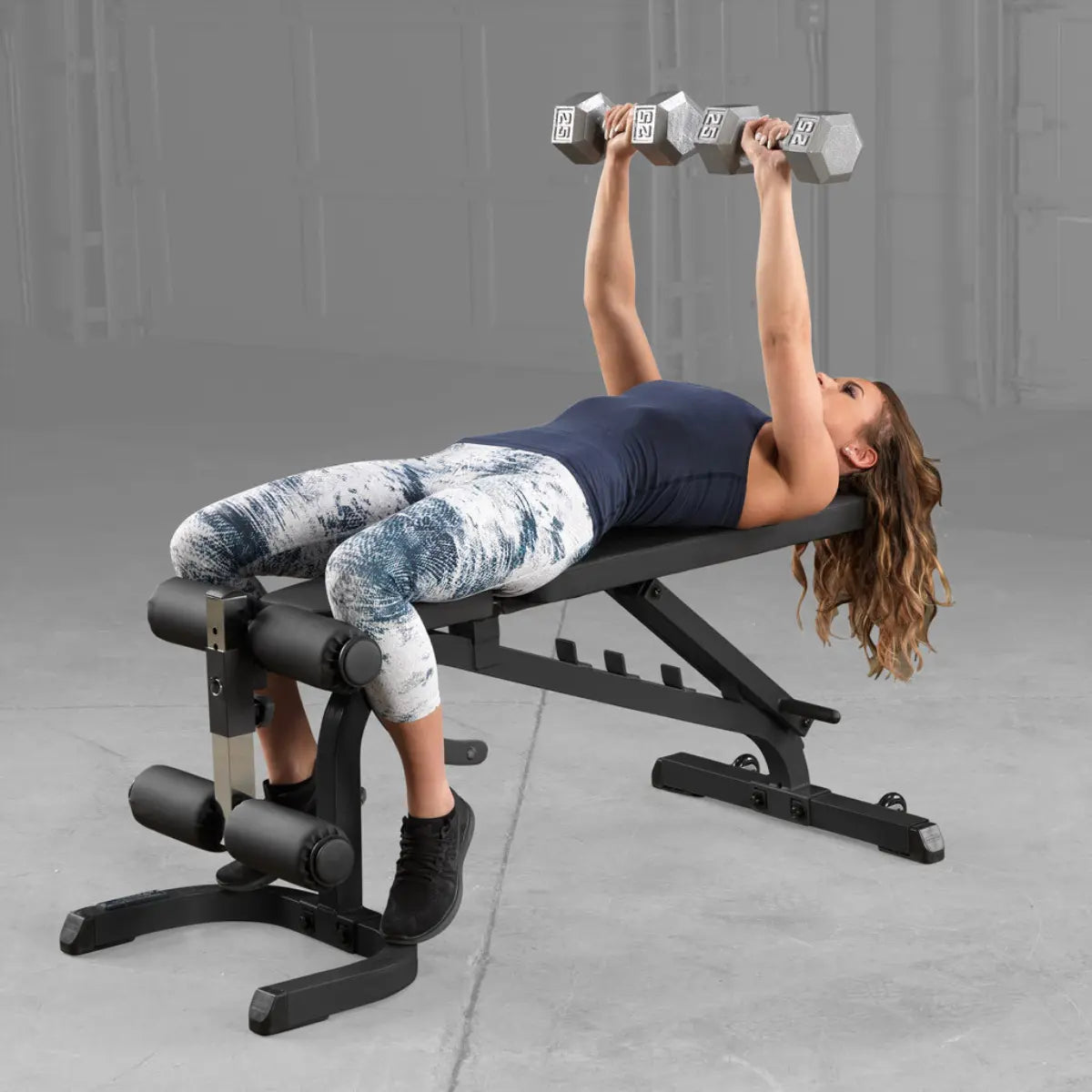 Vrouw ligt op een verstelbare trainingsbank en duwt twee halters omhoog.