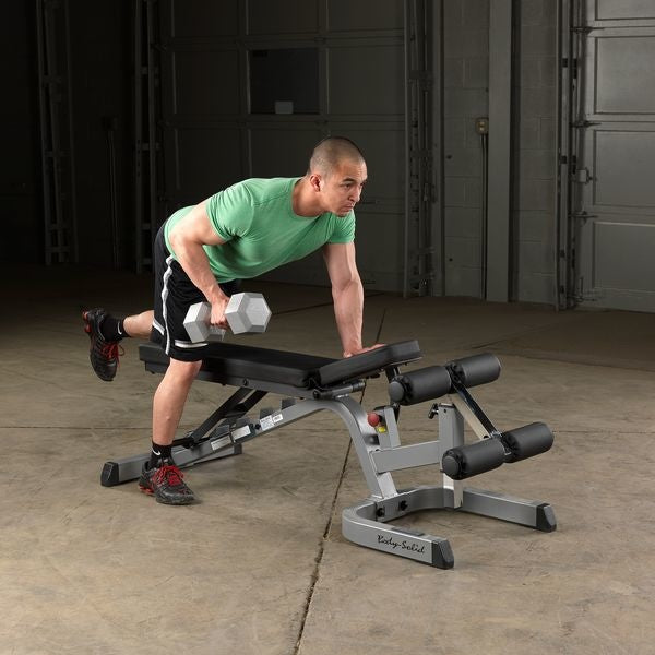 Man in groen shirt steunt met één hand op de bank en roeit met een dumbbell.