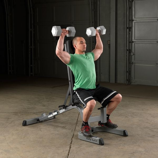 Man zit op een verstelbare bank en houdt twee dumbbells boven zijn hoofd.