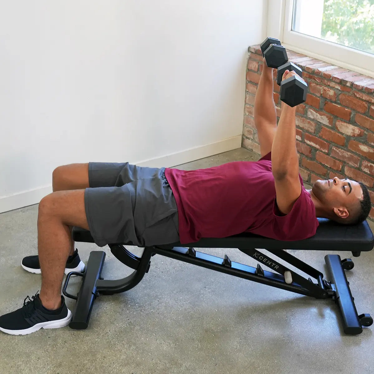 Man ligt op een trainingsbank en drukt twee dumbbells omhoog.