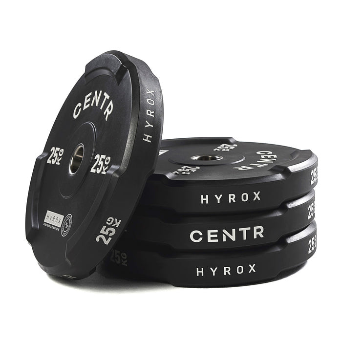 Een zwarte bumperplate leunt tegen een stapel plates; ‘CENTR’, ‘HYROX’ en ‘25 KG’ zijn zichtbaar.
