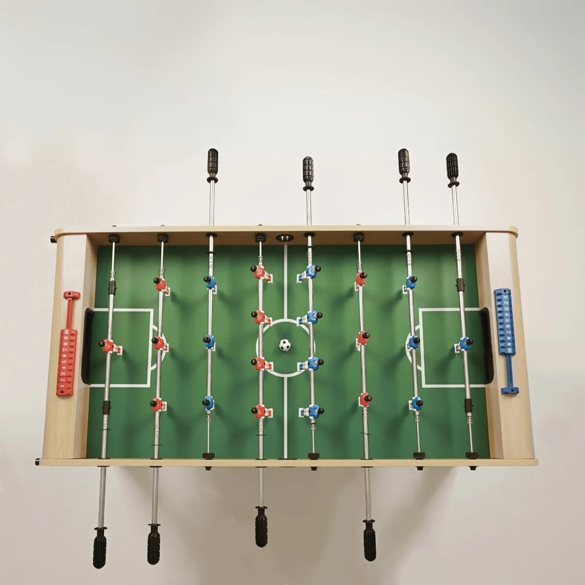 Bovenaanzicht van een groen voetbalveld met rode en blauwe spelers en speelstangen.