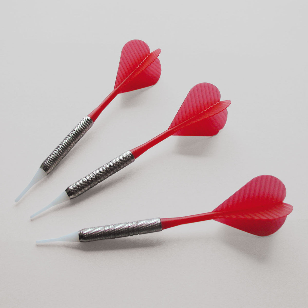 Drie darts met rode flights liggen op een lichte achtergrond.