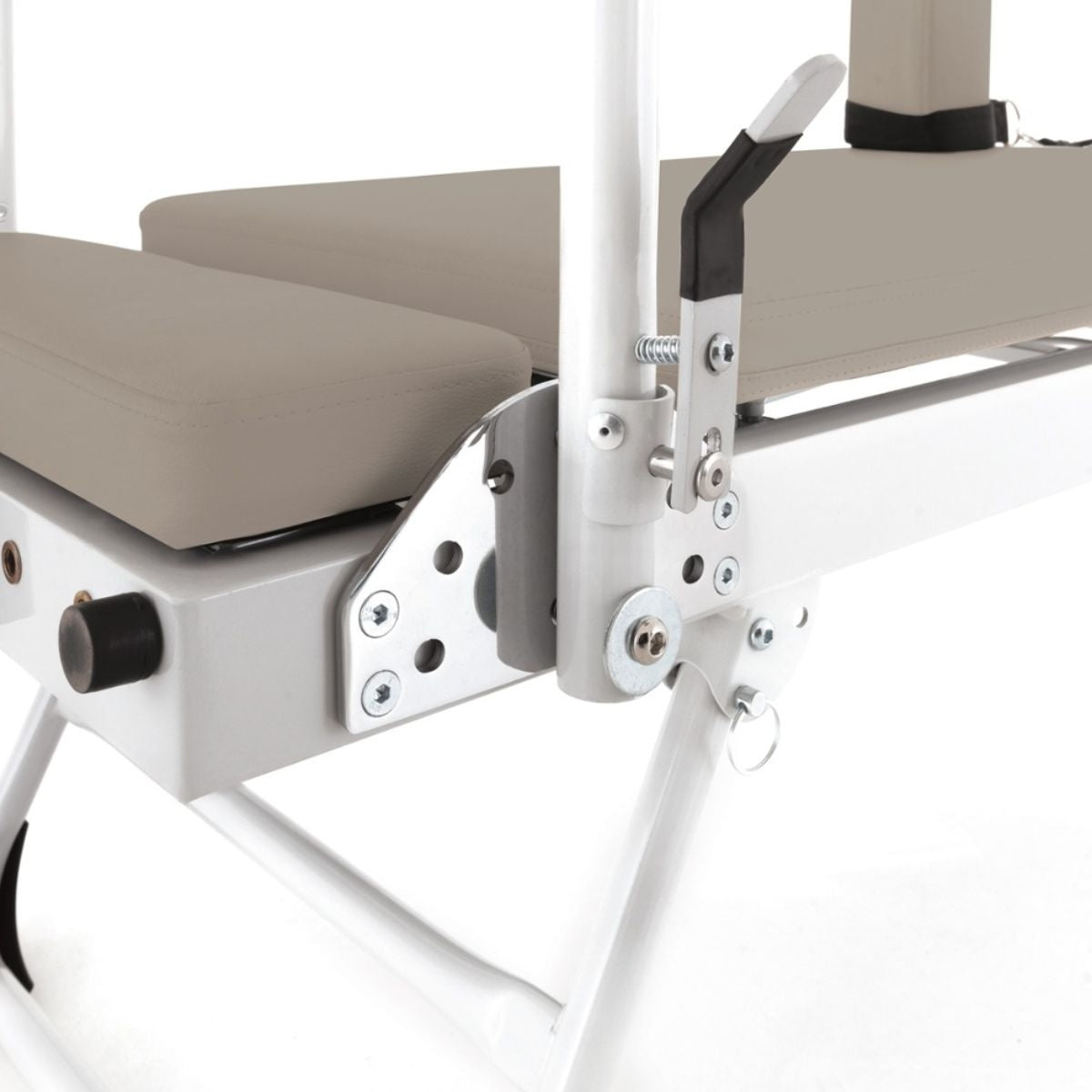Close-up van de witte reformersteun en verstelbare metalen onderdelen naast het zandkleurige bed.