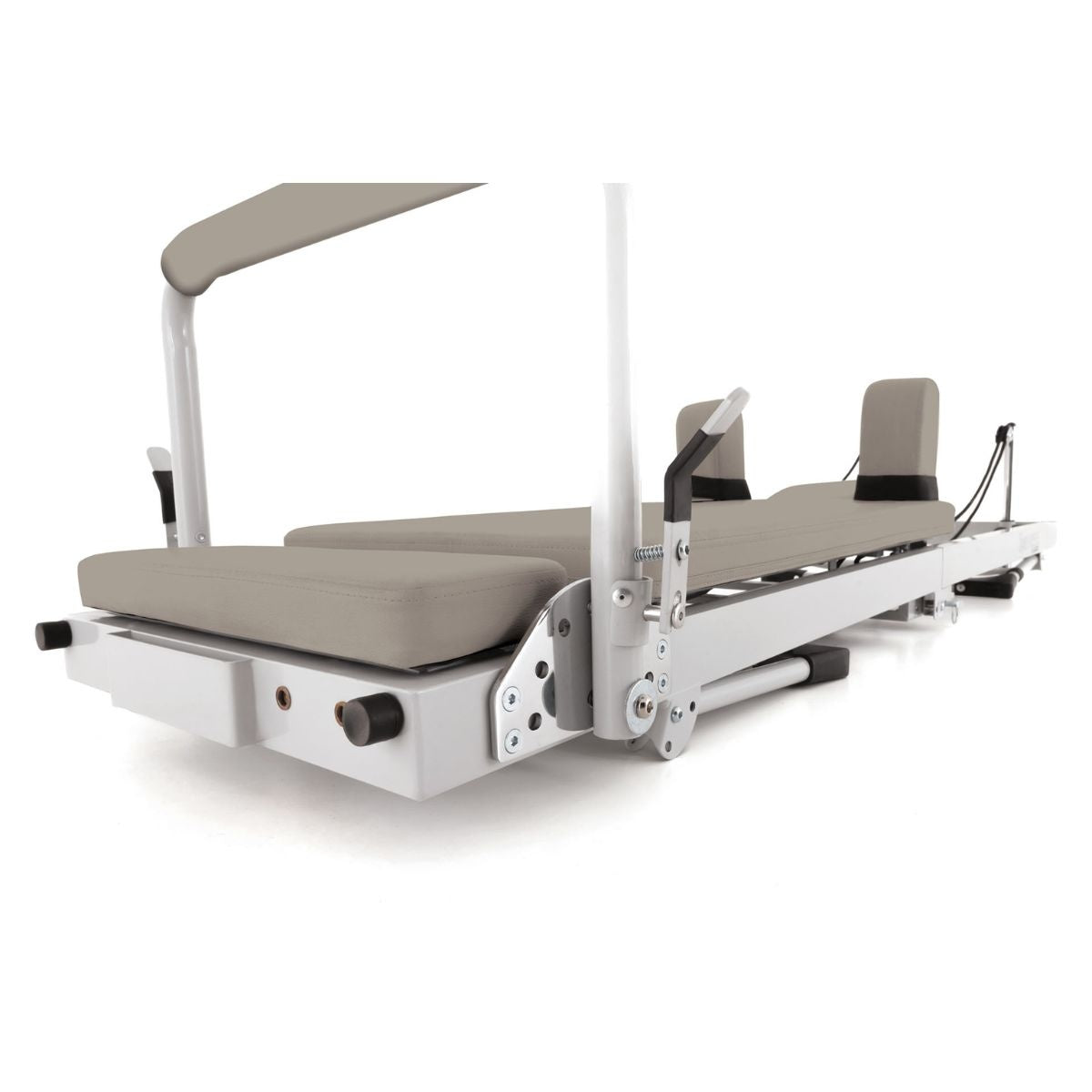 Zandkleurige pilatesreformer met witte torenconstructie, van opzij gezien.