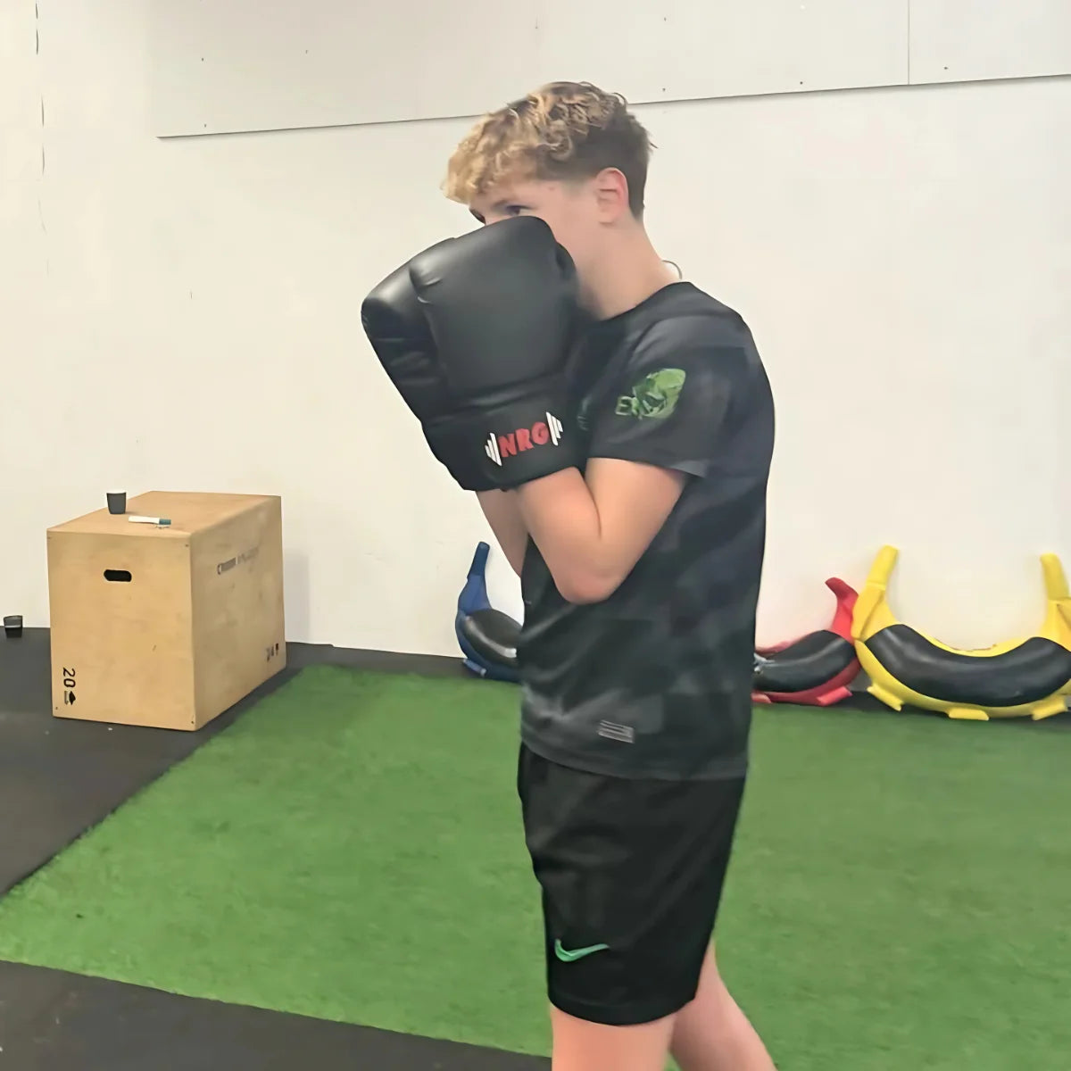 Man draagt zwarte NRG F4 bokshandschoenen in een fitnessruimte