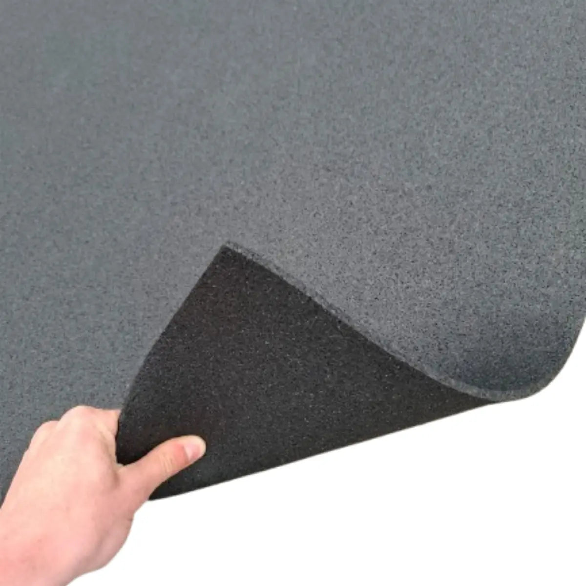 A hand lifts a corner of a black exercise mat to show its thick, dark gray underside.