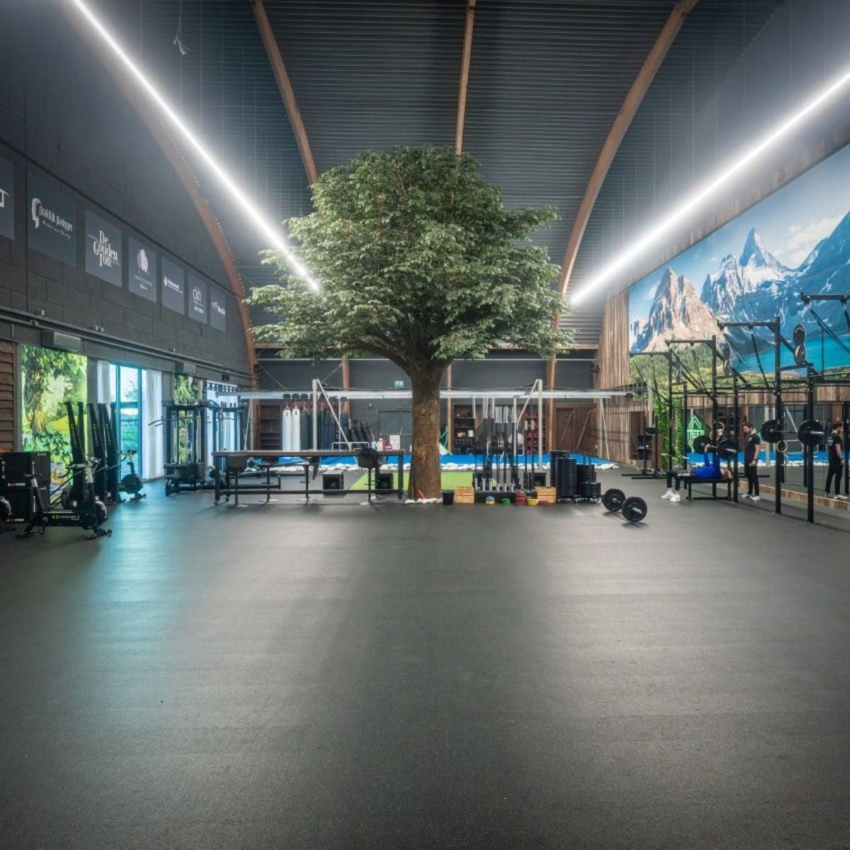 Ruime sportschool met een zwarte rubberen vloer, fitnessapparatuur en lange plafondverlichting.