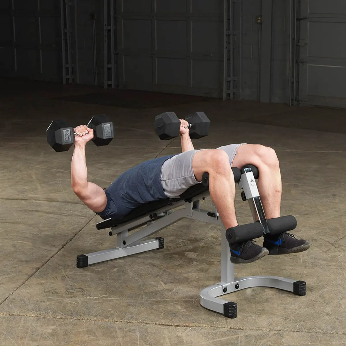 Man ligt op trainingsbank en houdt twee dumbbells boven zijn borst.