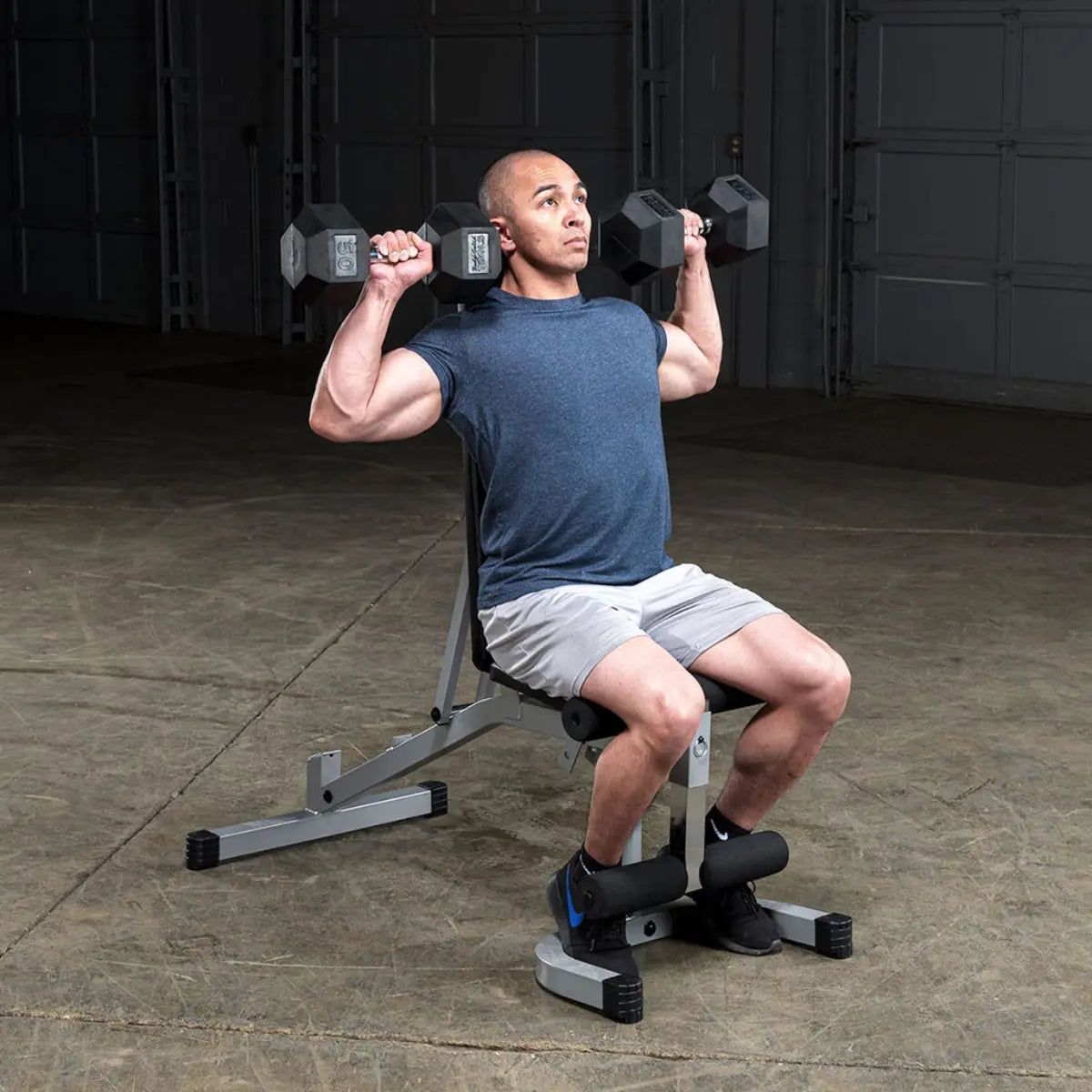 Man zit op schuine bank en duwt twee dumbbells boven zijn hoofd.