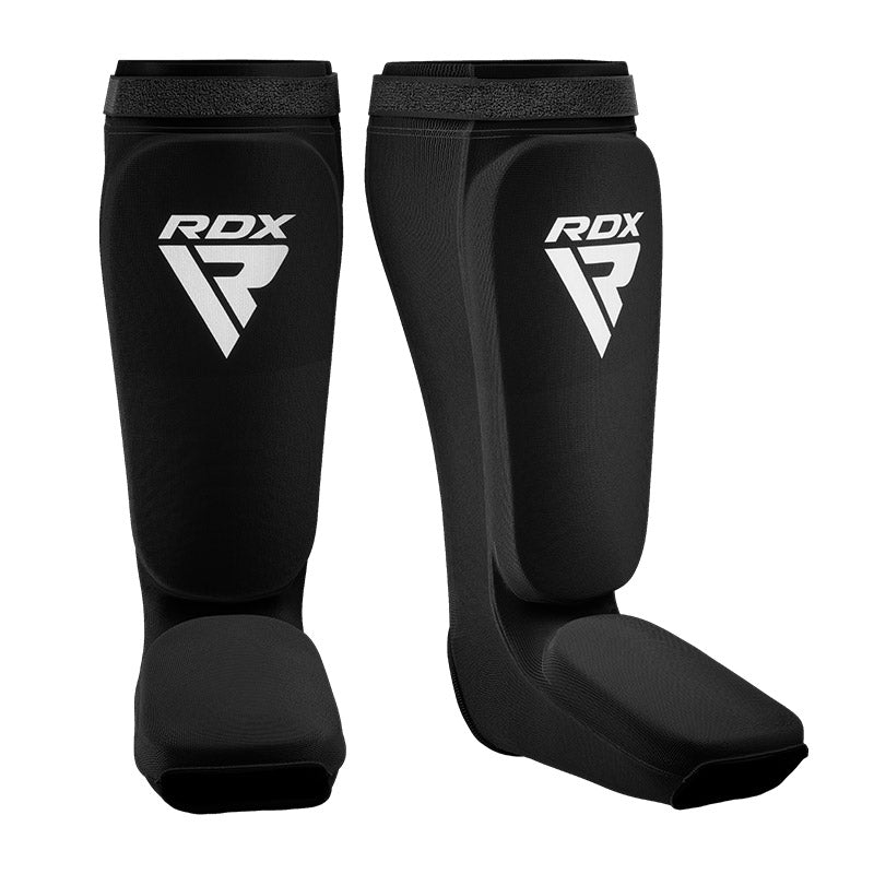A pair of black shin and instep guards with white RDX logos against a white background.