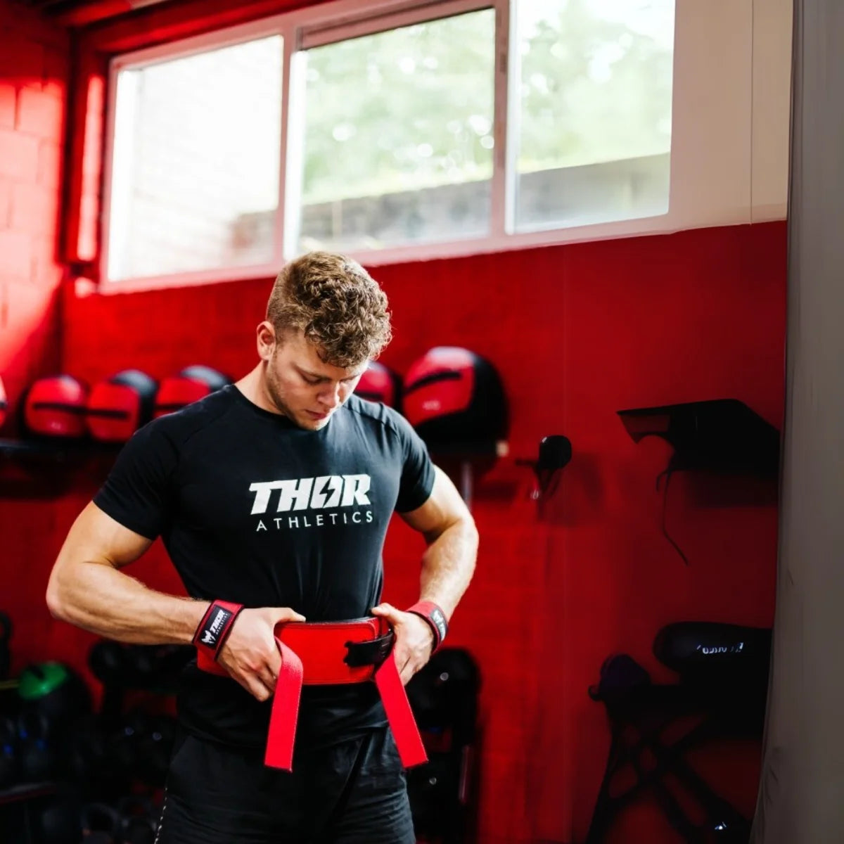 Man in zwart Thor Athletics-shirt houdt een rode riem vast in een sportschool.