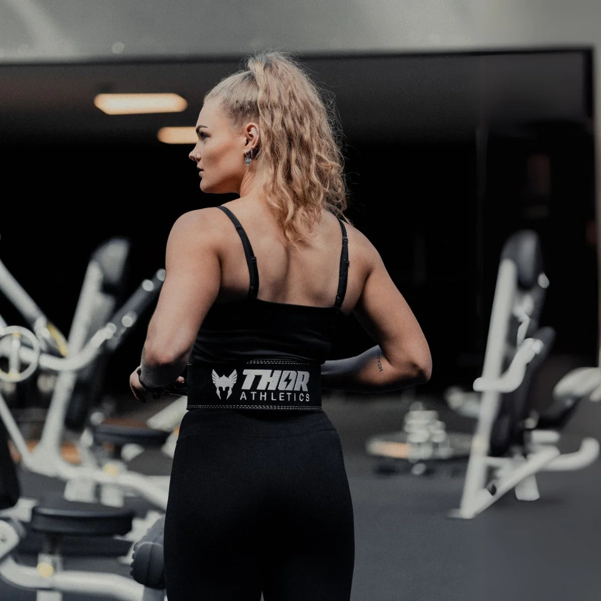Vrouw in zwarte sportkleding met een brede zwarte riem in een sportschool.