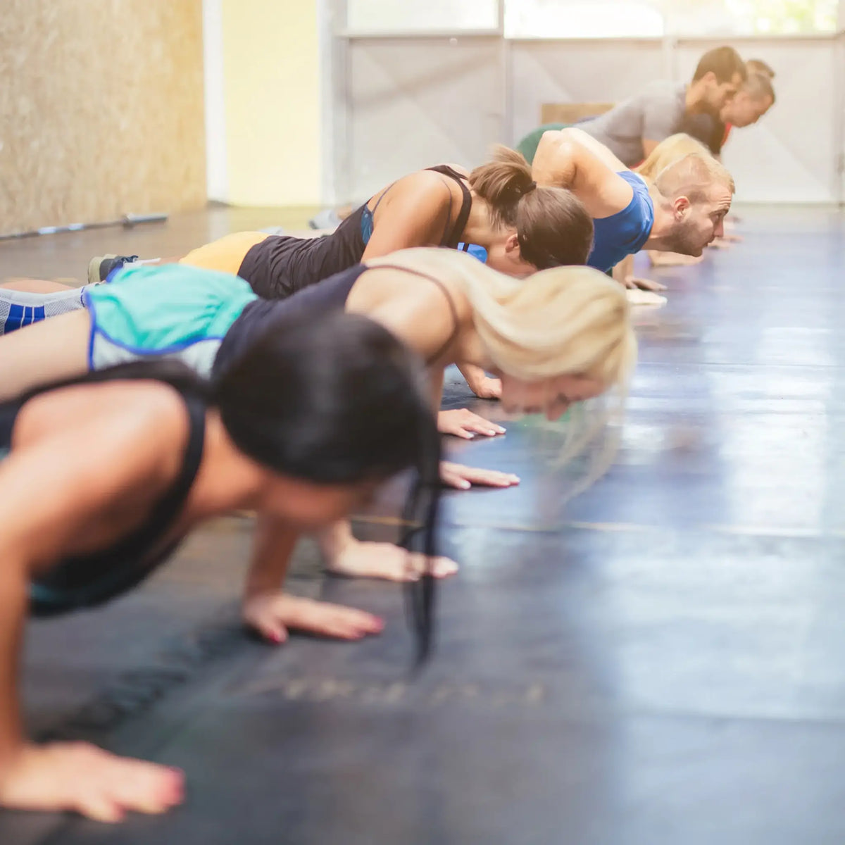 Rij sporters doet push-ups naast elkaar op de vloer van een fitnessstudio.