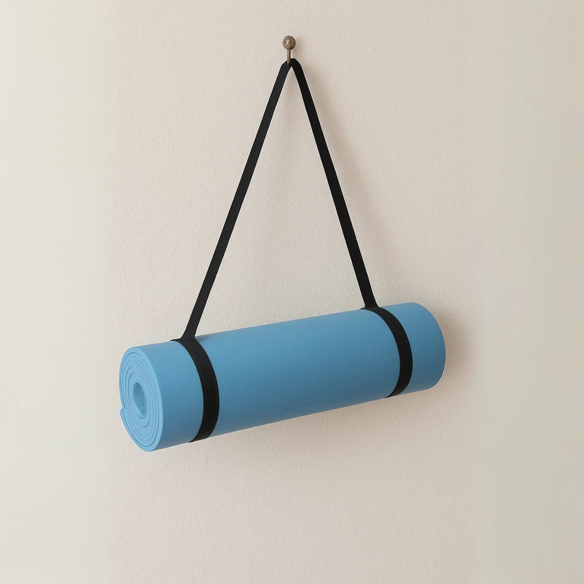 Opgerolde blauwe fitnessmat hangt aan een zwarte draagriem.