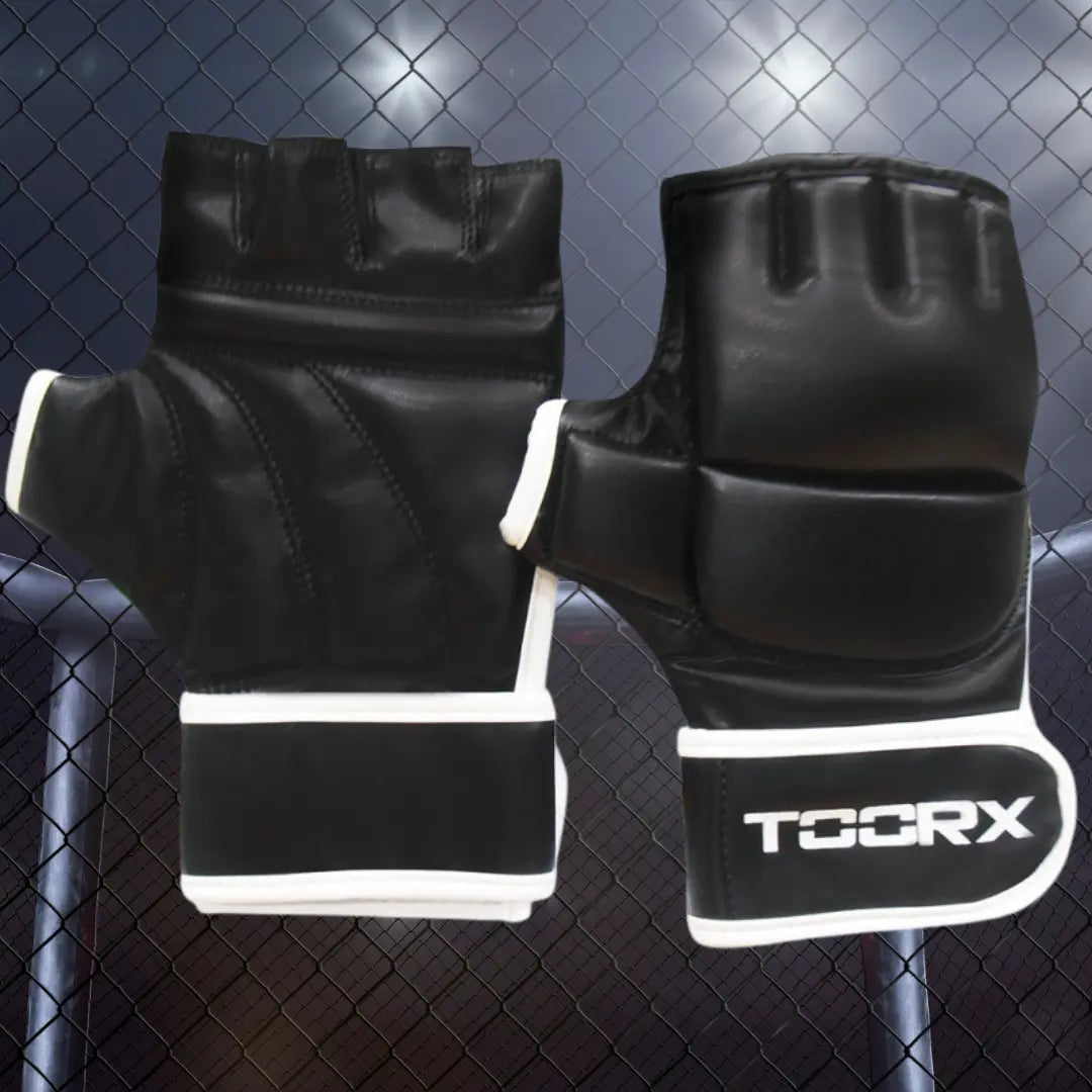 Zwarte MMA-handschoenen met open vingers en witte TOORX-logo’s tegen een donkere achtergrond met gaashek.