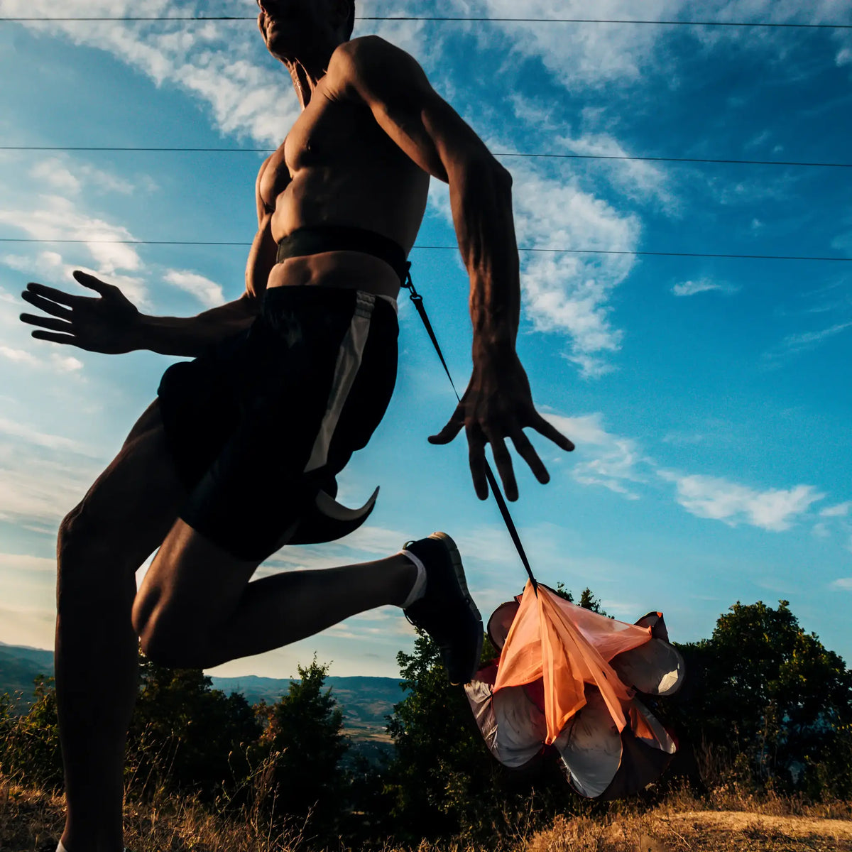 Atleet sprint buiten met een oranje weerstandsparachute achter zich.