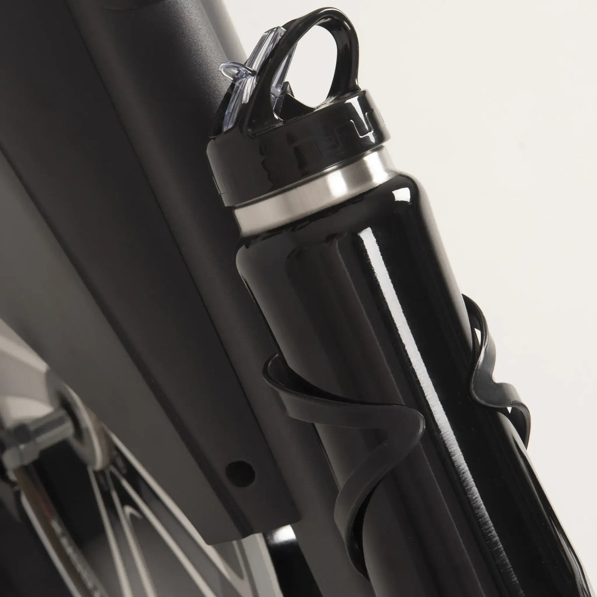 Bidon in een zwarte bidonhouder aan het frame van een spinningfiets.