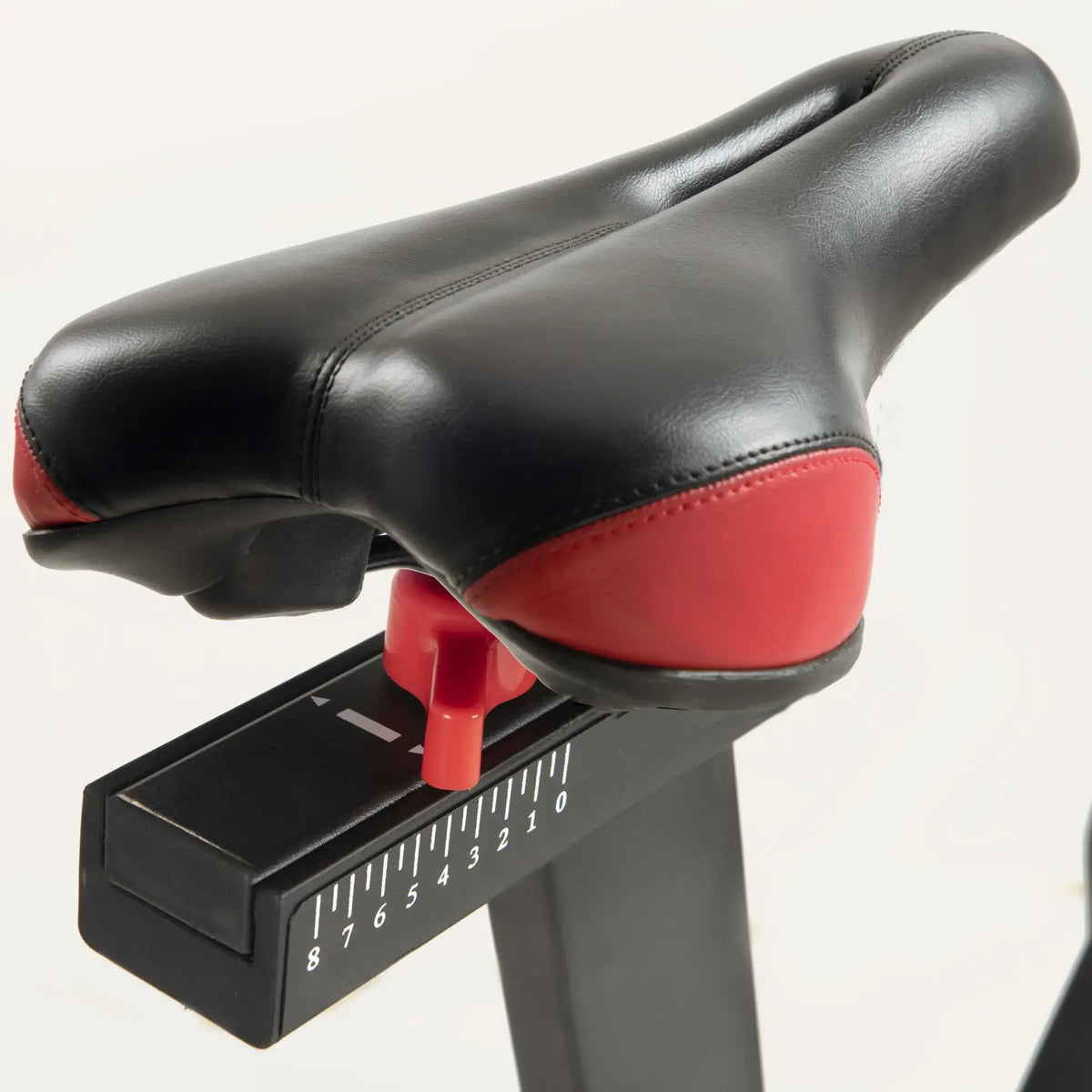 Zwart zadel met rode onderzijde op de verstelbare zadelpen van een spinningfiets.