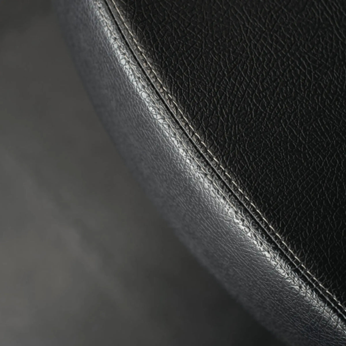 Close-up van zwart getextureerd kunstleer met een gebogen gestikte naad.