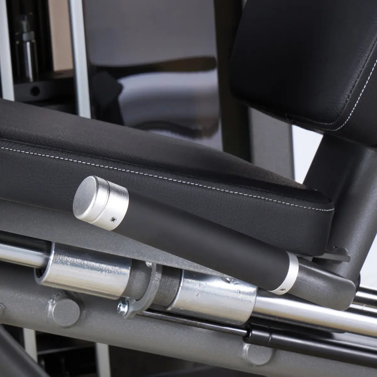 Close-up van de rolsteun en verstelgreep onder de zitting van een leg extension-machine.